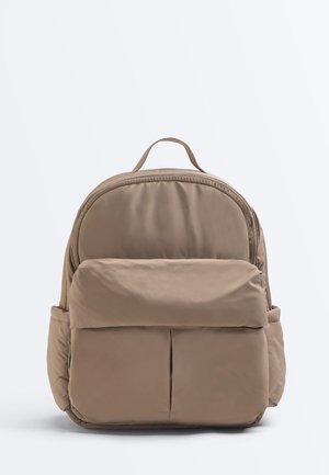 Beiger gepolsterter Rucksack mit vorderer Reißverschlusstasche, zwei Seitentaschen, oberem Griff und abgerundetem Reißverschluss.