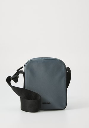Borsa a tracolla grigia in nylon dalla forma piatta, con una tracolla nera regolabile e un logo discreto sulla parte frontale. Texture liscia.