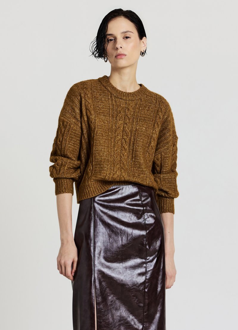 Brauner Strickpullover mit Zopfmuster, gerippten Bündchen und Saum, kombiniert mit einem hoch taillierten, glänzenden bordeauxfarbenen Rock mit seitlichem Schlitz.