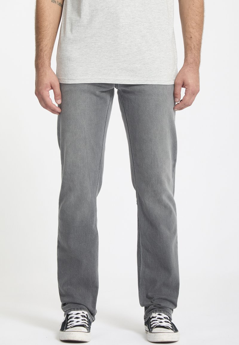 Slim-fit gray denim jeans with a faded texture, standard pockets, and stitched detailing, paired with black and white sneakers.