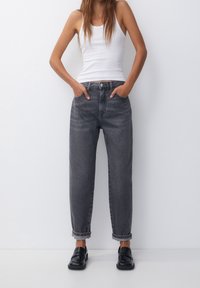 Mörkgrå denimjeans med avslappnad passform, uppvikta ärmar och sidofickor, i kombination med en vit linne och svarta loafers.