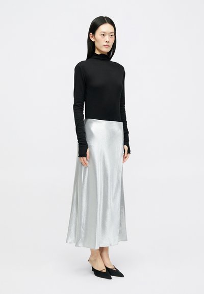 Črna dolga majica s turtleneck ovratnikom v kombinaciji z sijočo srebrno maksi krilo. Obleka dopolnjena z črnimi čevlji s koničastim nosom.