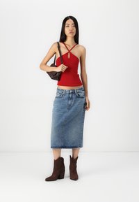 Top tipo tank de rayas rojas con tirantes en cruz, falda de mezclilla azul de cintura alta y botas marrones hasta el tobillo. Bolso marrón. Fondo minimalista.