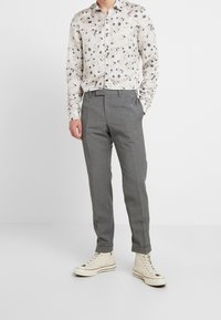 White floral shirt with small blue and purple patterns, paired with gray tailored trousers and beige high-top sneakers.