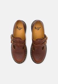 Brązowe skórzane buty z detalami w postaci klamry, perforowaną cholewką i żółtymi szwami na czarnej podeszwie. Charakteryzują się okrągłym noskiem.