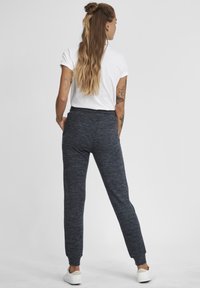 Tumed hallid tekstuuriga dressipüksid, vormitud siluetiga, elastse vöökoha ja kinnitusega pahkluude juures, koos valge lühikese käisega särgiga.