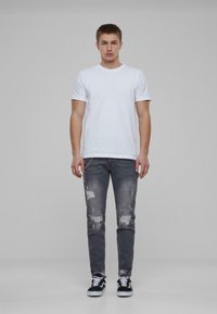 Hvit bomull t-skjorte, slim-fit, parret med mørkegrå slitte jeans med rifter og en sølvkjede-detalj; svarte joggesko med hvite såler.