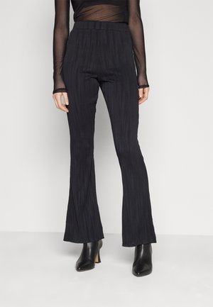 Pantalones acampanados de talle alto en negro con textura, combinados con botines negros de tacón y una blusa translúcida de manga larga.