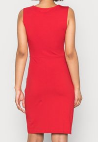 Červené šaty bez rukávů s přiléhavým střihem, vyrobené z elastické látky. Mají kulatý výstřih a hladkou texturu, zasahující nad kolena.