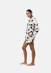 Set di loungewear leggero di colore crema con motivo di gatti neri, composto da una maglia con bottoni e pantaloni corti abbinati, dotato di tasche laterali.