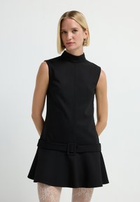 Schwarzes ärmelloses Kleid mit hohem Ausschnitt, tailliertem Oberteil und ausgestellt Rock, versehen mit einem breiten Gürtel mit rechteckiger Schnalle. Texturierten Hintergrund.