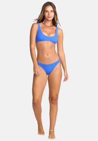 Niebieski bikini z prążkowanej tkaniny, zawierający top w stylu braletki z szerokimi ramiączkami oraz dopasowane majtki w niskim stanie, zaprojektowany dla podkreślenia sylwetki.