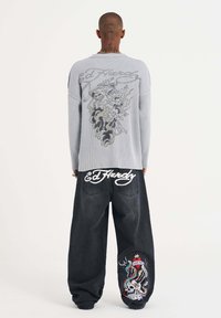 Gray ribbed sweater with a detailed graphic on the back; black jeans featuring colorful embroidery and "Ed Hardy" branding on the waistband.