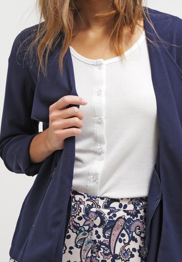 Veste ouverte marine portée sur un haut blanc côtelé à boutons, associée à un pantalon à motifs floraux et cachemire en bleu et rose.
