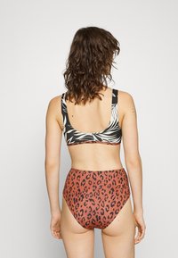 Fekete-fehér levélmintás melltartóból és magasan szabott, rozsdaszínű alsóból álló bikini szett, fekete leopárdmintával. Sima szövettextúra.
