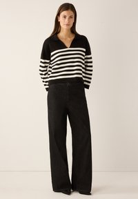 Zwart-wit gestreepte gebreide trui met een kraag; gecombineerd met zwarte, wijde jeans met een hoge taille en puntige zwarte schoenen.