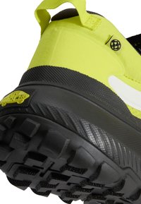 Gros plan d'une semelle de chaussure de randonnée jaune néon et noire avec des crampons profonds et une languette de traction au talon.