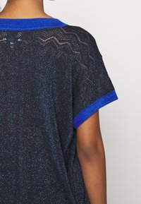 Czarna dzianinowa bluzka z teksturowanym wzorem, niebieską prążkowaną kołnierzem i mankietami, subtelnie błyszcząca. Luźny krój i krótki rękaw.