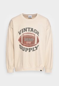 Béžová mikina s grafickým motivem fotbalu ve vintage stylu a textem "Vintage Supply 1991" na přední straně, dlouhé rukávy, kulatý výstřih.