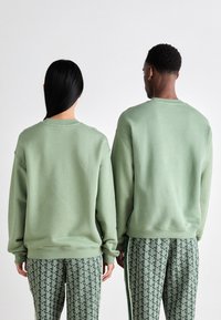 Green crewneck sweatshirts with ribbed cuffs and hem, paired with patterned green pants featuring a geometric design. Rear view.