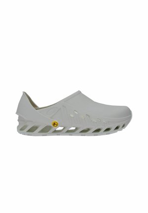 Zapato blanco sin cordones con suela ventilada y aberturas laterales para la transpirabilidad, con un pequeño logotipo circular amarillo cerca del talón.