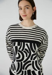 Zwart-wit gestreept sweater met een geometrisch patroon op de onderste helft. Heeft lange mouwen en een ronde halslijn. Zachte textuur.