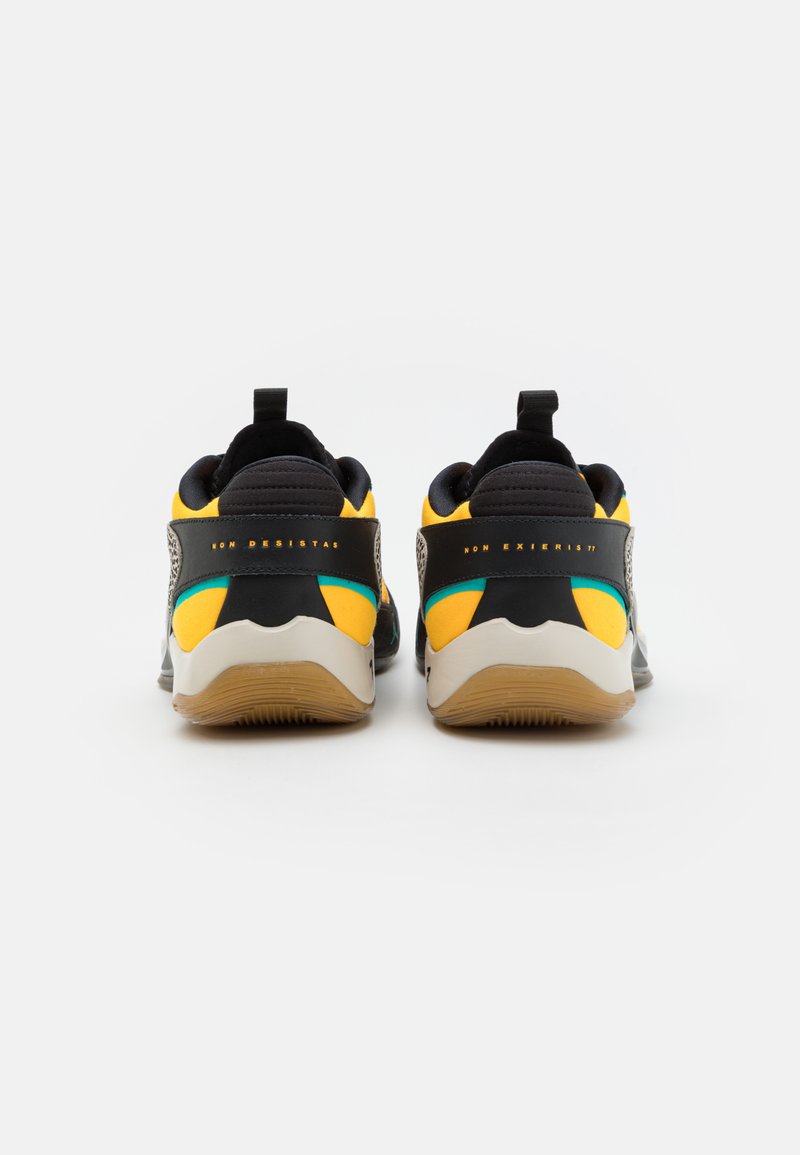 Baskets de sport noires et jaunes avec un matériau texturé, un talon renforcé et une semelle en caoutchouc. Présentent une languette de tirage et des couleurs d'accent en teal.