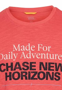 Rød kortærmet t-shirt lavet af et blødt, tekstureret stof med hvid og sort tekst: "Made For Daily Adventure" og "CHASE NEW HORIZONS."