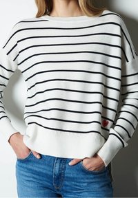 Weißer Pullover mit schwarzen Streifen, Rundhalsausschnitt und geripptem Saum. Verfügt über einen kleinen roten Herzakzent auf der linken Seite.