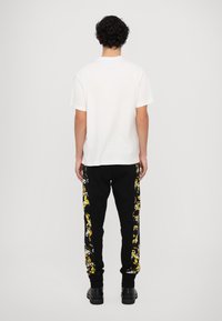 Balta īsajām piedurknēm t-kreklā, apvienota ar melniem sporta biksēm, kuru malās ir dzeltenā un baltā ziedu raksts, pabeigta ar melnām zābakām.