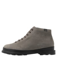 Bottines en cuir suédé gris avec un bout rond, des lacets marron et une semelle en caoutchouc noire. Présente un détail de couture discret près du bout et une étiquette de logo.