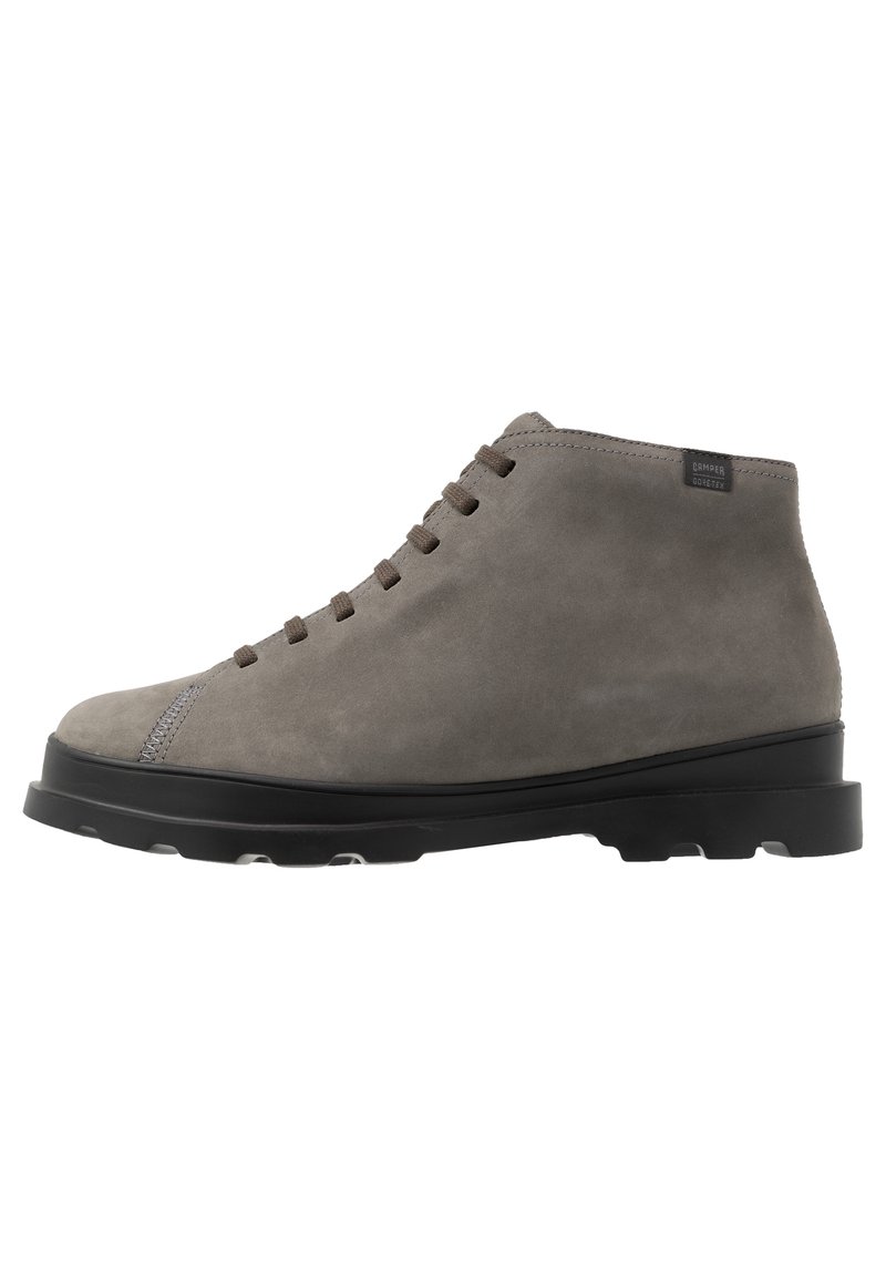 Bottines en cuir suédé gris avec un bout rond, des lacets marron et une semelle en caoutchouc noire. Présente un détail de couture discret près du bout et une étiquette de logo.