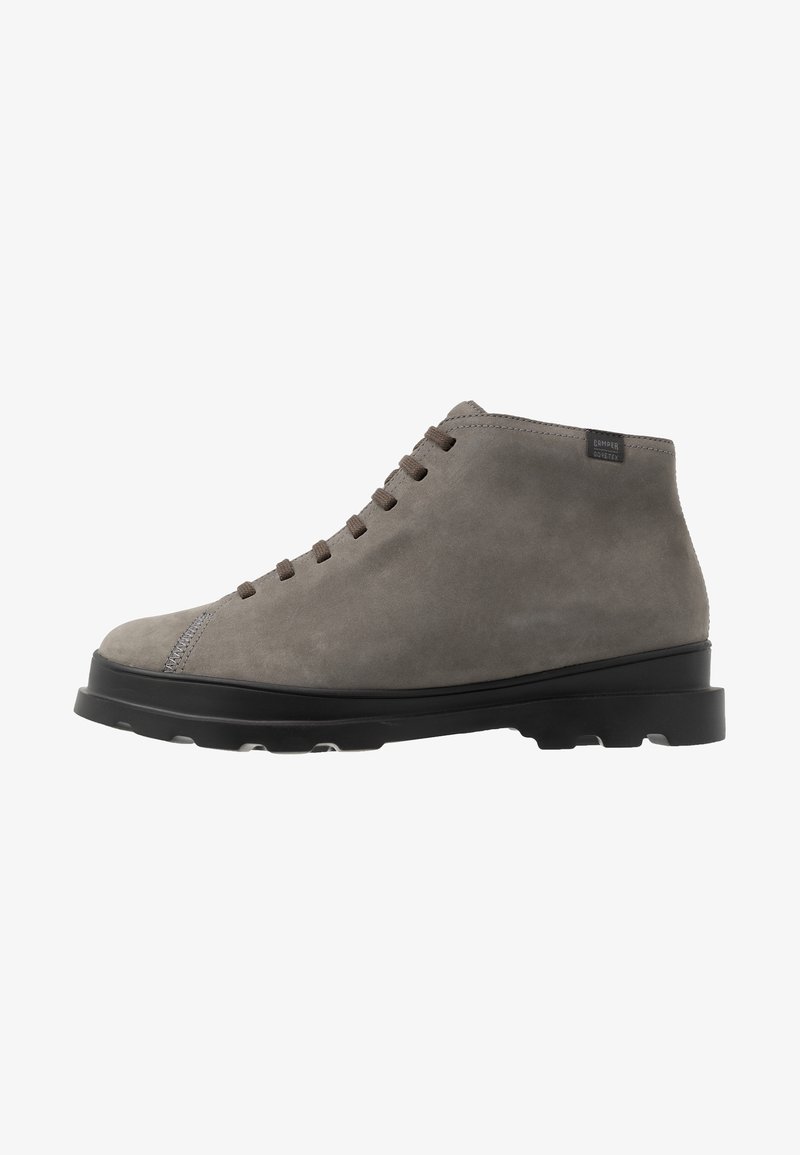 Bottines en cuir suédé gris avec un bout rond, des lacets marron et une semelle en caoutchouc noire. Présente un détail de couture discret près du bout et une étiquette de logo.