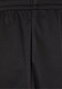 Gros plan d'un tissu noir texturé avec de petites perforations et une couture verticale visible.