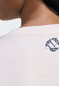 Světle barevné bavlněné tričko s námořnicky modrým grafickým motivem na zadní straně u krku. Žebrovaný límec a jemná textura.