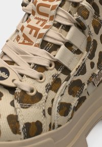 Baskets beige avec imprimé léopard marron, lacets crème et étiquettes de marque sur la languette et le côté près de la semelle épaisse.