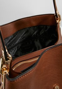 Brown leather handbag with a textured exterior, black fabric lining, gold zipper, and an internal zip pocket.