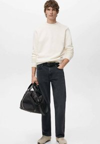 Sudadera blanca, vaqueros negros, zapatos beige, sosteniendo un bolso negro de diseño elegante. Textura suave, ajuste casual y paleta de colores neutros.