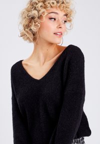 Sort v-hals sweater i blødt, tekstureret stof og løs pasform. Har lange ærmer og en afslappet silhuet, parret med mønstrede bukser.
