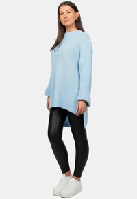 Maglione lavorato a maglia azzurro chiaro con maniche lunghe, texture a coste e spacchi laterali, abbinato a leggings neri lucidi e sneaker bianche.
