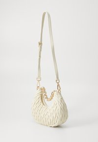 Bela tkanina torba v obliki lune, opremljena z zlatim verižnim poudarkom in nastavljivim trakom, izdelana iz teksturiranega materiala. Zadrga kot podrobnost.