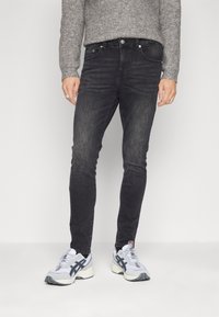 Jeans de mezclilla negros con un corte ajustado, que presentan un diseño clásico de cinco bolsillos, detalles de desgaste y combinados con zapatillas de correr en blanco y gris.