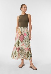 Grüner gerippter Tanktop kombiniert mit einem Maxirock, der mit einem floralen Diamantmuster in Rosa, Orange und Grüntönen gestaltet ist. Flache Riemchensandalen.