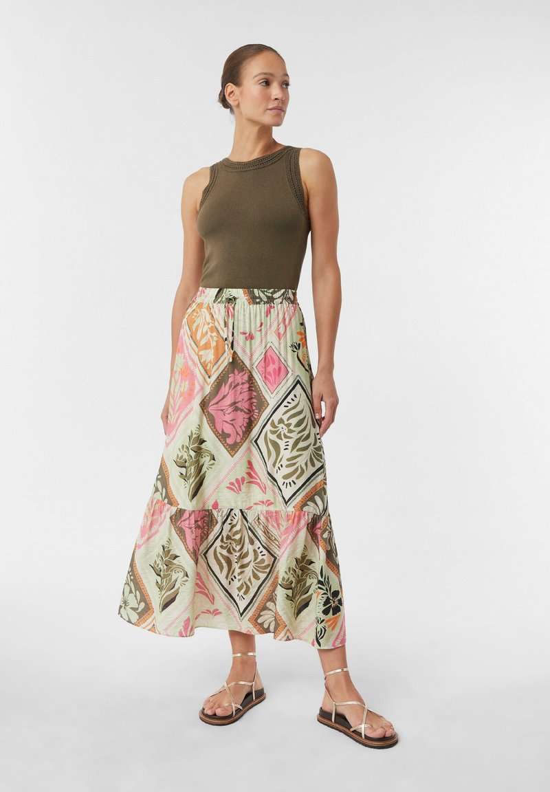 Grüner gerippter Tanktop kombiniert mit einem Maxirock, der mit einem floralen Diamantmuster in Rosa, Orange und Grüntönen gestaltet ist. Flache Riemchensandalen.
