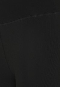 Schwarze Leggings aus dehnbarem Material, mit nahtloser Verarbeitung und geripptem Muster an den Seiten für zusätzlichen Detailreichtum.