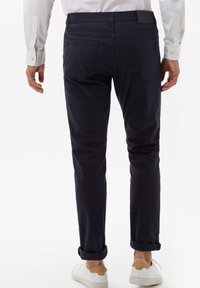 Marinblå bomullsbukser med tapered passform, med uppvikta fållar och en samtida midja. Bakfickor är synliga, med läderbranding.