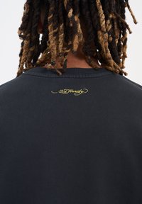 Svart sweatshirt med rund halsringning som har en broderad gul logotyp på baksidan. Slät textur och normal passform, med ribbat halsband.