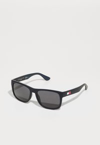 Gafas de sol rectangulares negras con lentes oscuros, que presentan un acento de logo en la patilla. Hechas de plástico con textura suave.