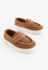 Bruna läderskor med slip-on-design och vävt mönster på tåboxen, en platt vit gummisula och en diskret remdetalj över fotryggen.
