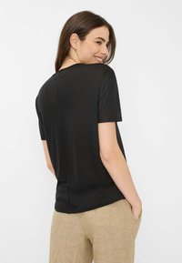 Sort kortærmet t-shirt med rund halsudskæring og en løs pasform, fremstillet af letvægtsstof. Har en sømdetalje langs ryggen.